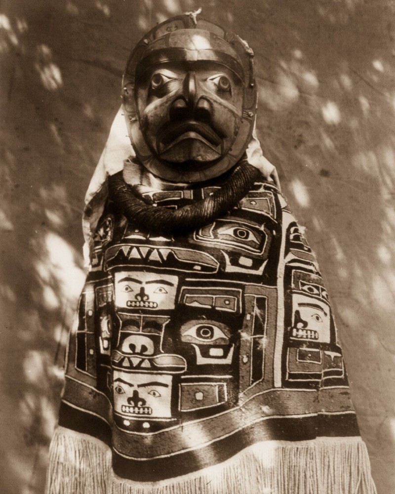 1914 A Qagyuhl woman wears a fringed Chilkat blanket and a mask representing a deceased relative who had been a shaman.